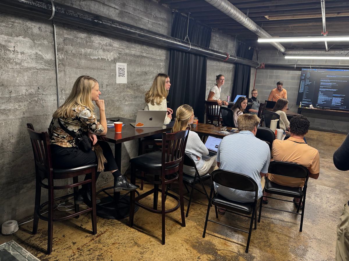 Students gather at a high table by the large screen downstairs for the set-up breakout.